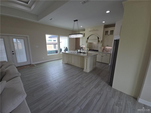 kitchen featuring french doors, a center island with sink, appliances with stainless steel finishes, decorative light fixtures, and light hardwood / wood-style floors