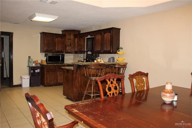 kitchen featuring a breakfast bar area, dark brown cabinetry, kitchen peninsula, and light tile patterned floors