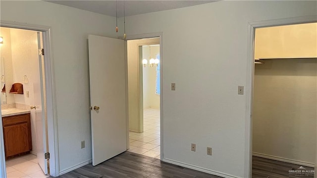 unfurnished bedroom featuring a spacious closet, ensuite bathroom, a chandelier, light hardwood / wood-style floors, and a closet