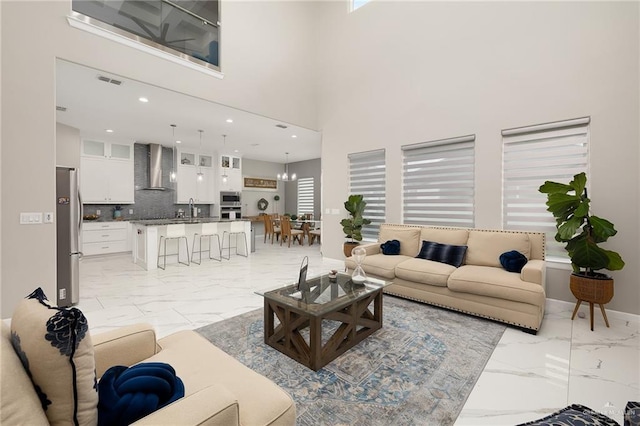 living room with a notable chandelier, a high ceiling, marble finish floor, visible vents, and recessed lighting