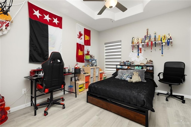 bedroom featuring baseboards, a tray ceiling, wood finished floors, and a ceiling fan