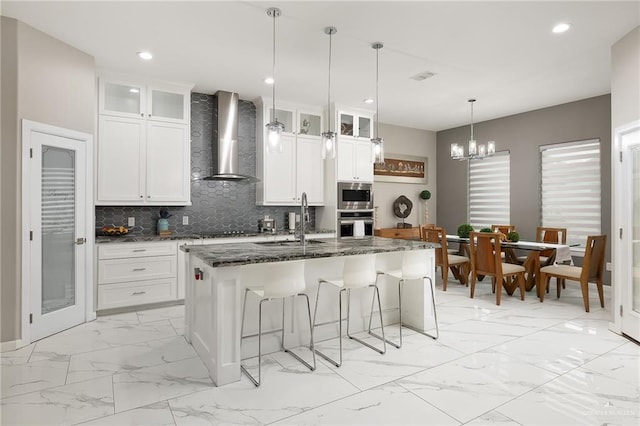 kitchen featuring a kitchen bar, marble finish floor, a sink, wall chimney range hood, and appliances with stainless steel finishes