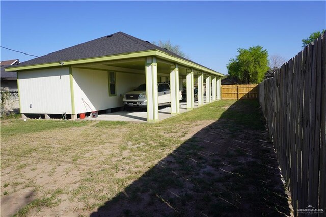 exterior space with an attached carport, roof with shingles, a yard, and a fenced backyard