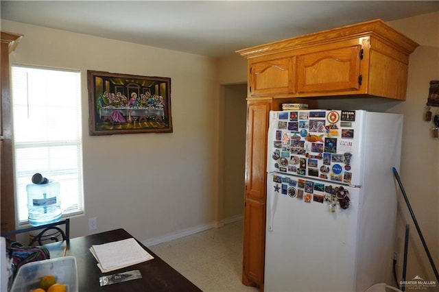 kitchen featuring light floors, baseboards, brown cabinets, and freestanding refrigerator