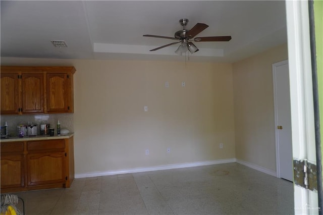 kitchen with baseboards, a raised ceiling, ceiling fan, brown cabinets, and light countertops