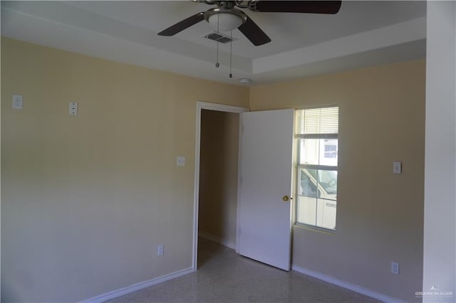 empty room featuring a raised ceiling, visible vents, ceiling fan, baseboards, and speckled floor