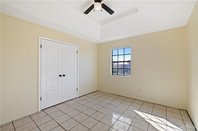 unfurnished bedroom with ceiling fan, a raised ceiling, a closet, and light tile patterned floors