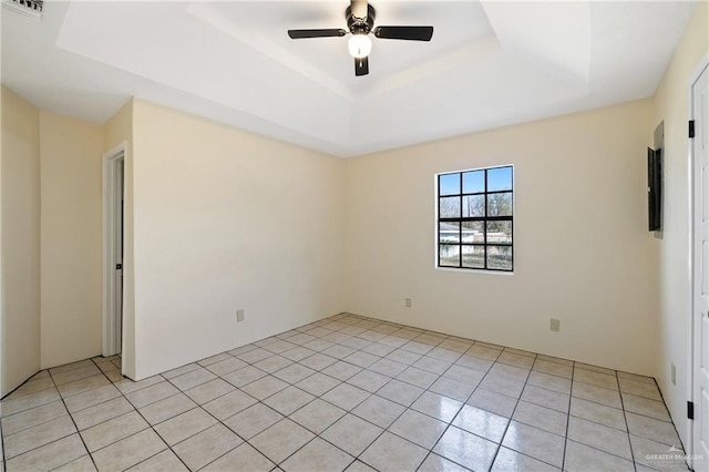 spare room with light tile patterned flooring, ceiling fan, and a raised ceiling