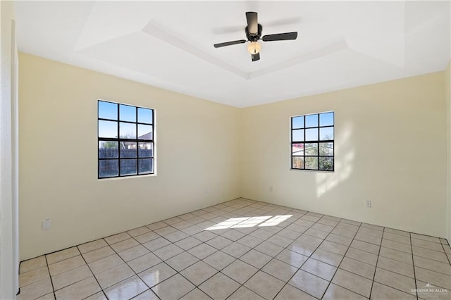 tiled spare room featuring ceiling fan and a tray ceiling