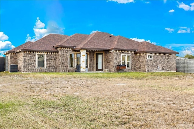 back of property with roof with shingles, central air condition unit, fence, brick siding, and a lawn
