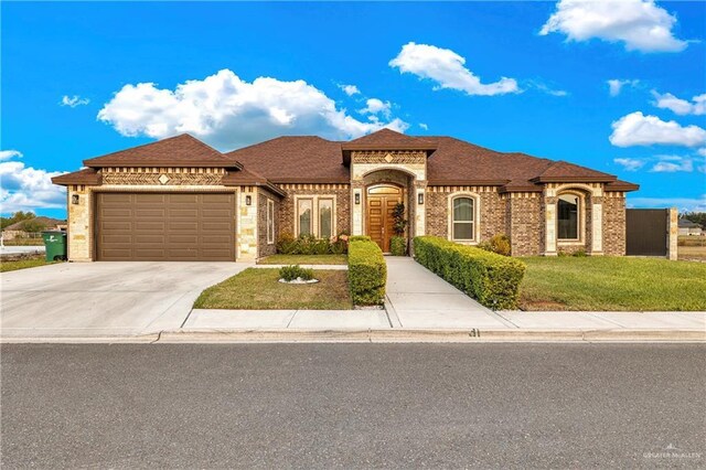 mediterranean / spanish home with concrete driveway, brick siding, a garage, a shingled roof, and a front yard