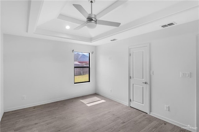 spare room featuring light wood-style flooring, visible vents, baseboards, a ceiling fan, and a raised ceiling