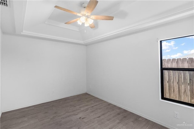 spare room featuring a ceiling fan, a tray ceiling, baseboards, and wood finished floors