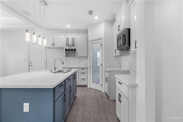 kitchen featuring glass insert cabinets, a sink, white cabinetry, light countertops, and a center island with sink