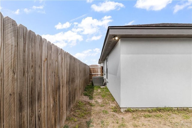 view of side of property with stucco siding, fence, and central AC unit