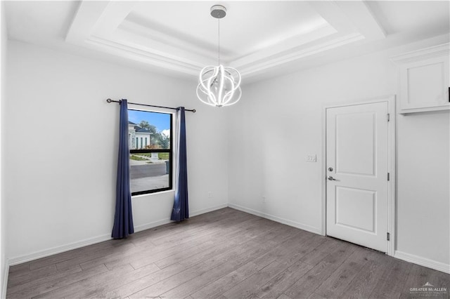 spare room featuring light wood finished floors, a tray ceiling, a chandelier, and baseboards