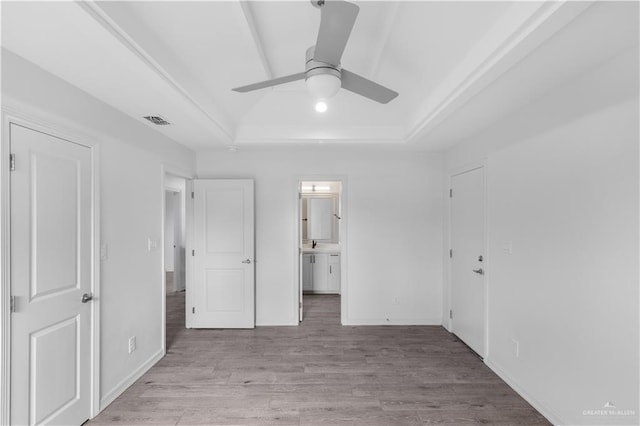 unfurnished bedroom featuring a tray ceiling, light wood finished floors, visible vents, ensuite bath, and baseboards