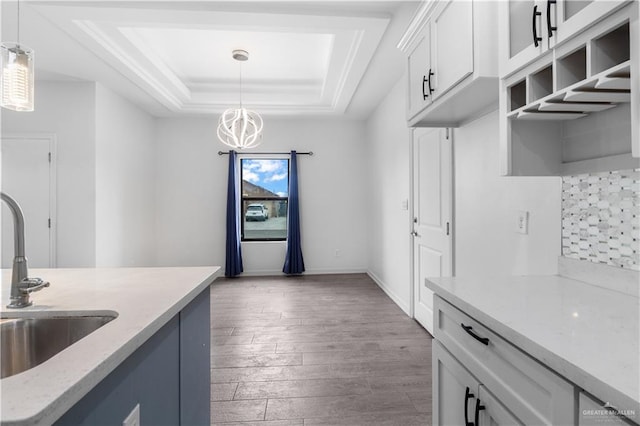 kitchen with a tray ceiling, hanging light fixtures, light wood-style flooring, white cabinetry, and a sink