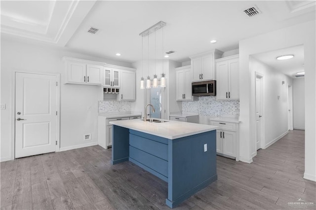 kitchen featuring light countertops, stainless steel microwave, glass insert cabinets, white cabinetry, and an island with sink