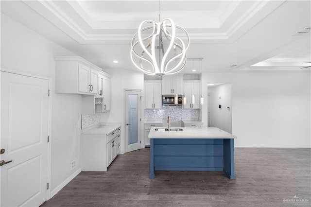 kitchen with white cabinets, light countertops, a tray ceiling, stainless steel microwave, and pendant lighting