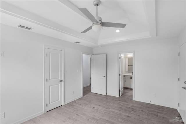 unfurnished bedroom with baseboards, visible vents, a raised ceiling, ensuite bathroom, and light wood-type flooring