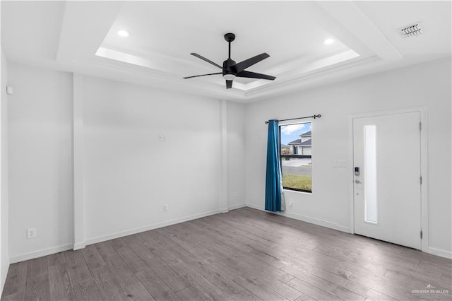 unfurnished room featuring visible vents, a raised ceiling, baseboards, ceiling fan, and light wood-style flooring