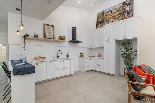 kitchen featuring white cabinetry, sink, wall chimney range hood, a kitchen breakfast bar, and pendant lighting