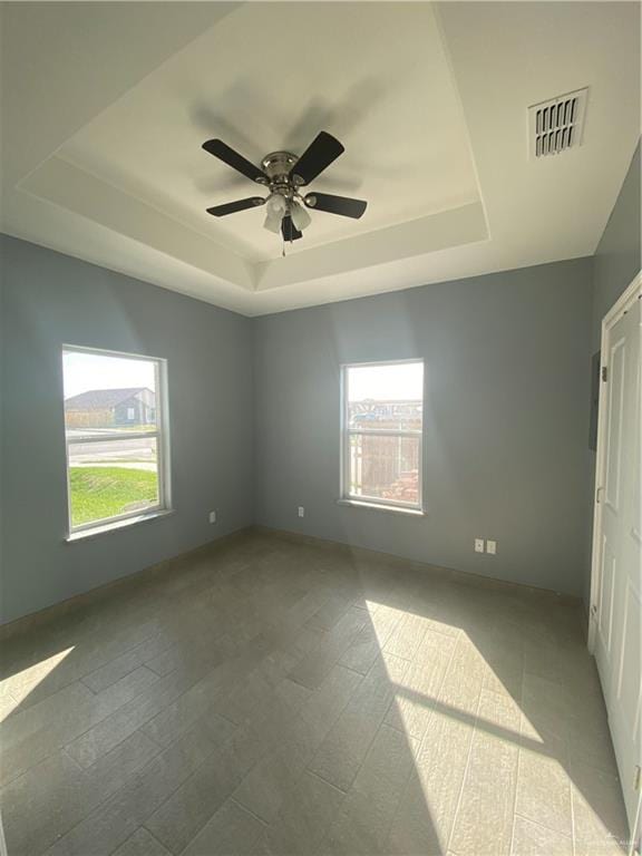 empty room featuring a tray ceiling, ceiling fan, and a healthy amount of sunlight