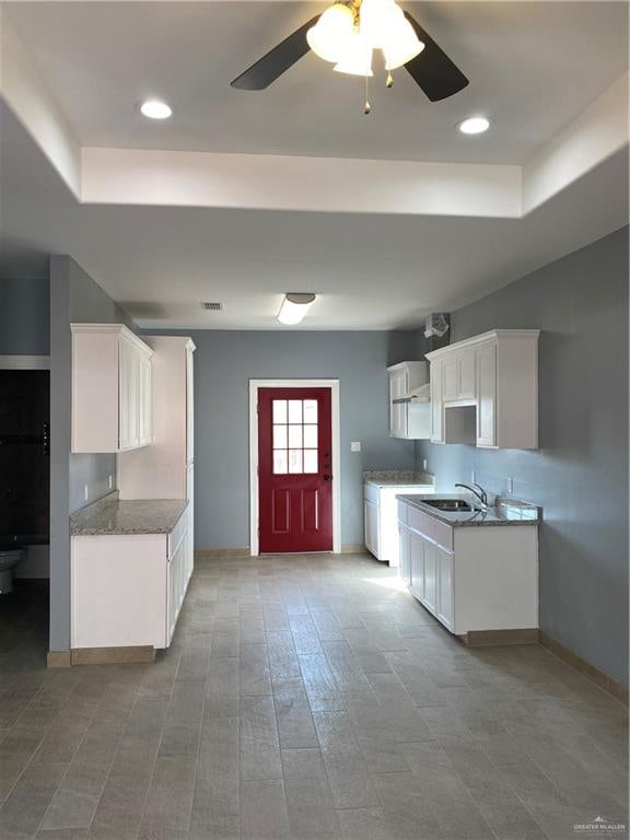 kitchen with ceiling fan, sink, light hardwood / wood-style floors, a tray ceiling, and white cabinets