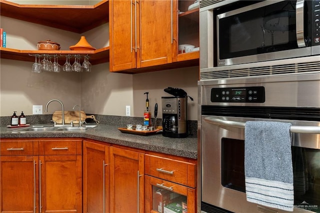 kitchen featuring brown cabinets, open shelves, dark countertops, appliances with stainless steel finishes, and a sink