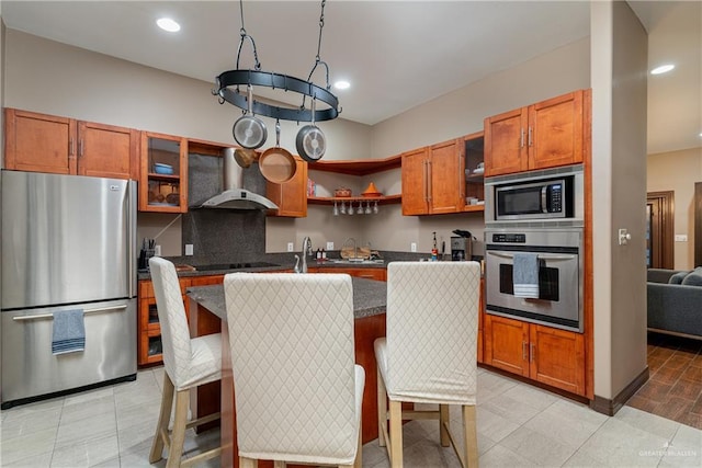 kitchen featuring stainless steel appliances, a kitchen island with sink, glass insert cabinets, and wall chimney range hood