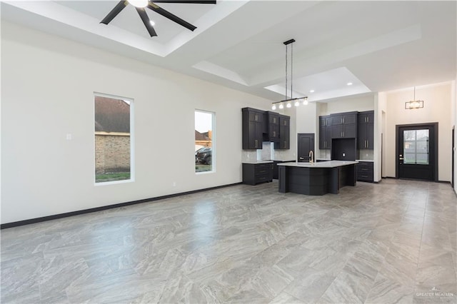 kitchen featuring pendant lighting, sink, ceiling fan, a kitchen island with sink, and a tray ceiling