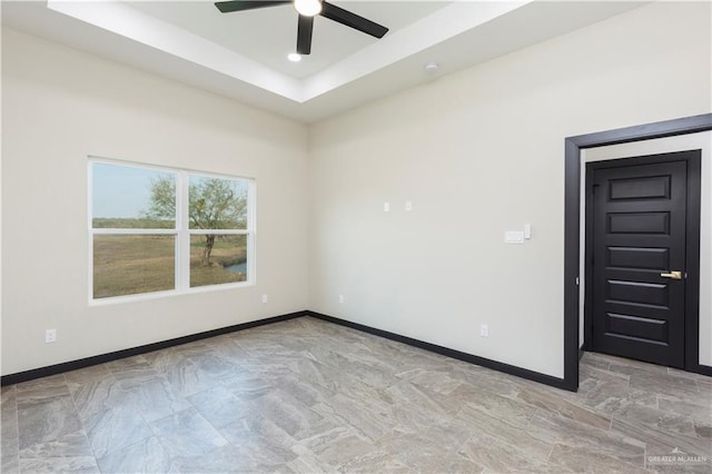 unfurnished room with ceiling fan and a tray ceiling