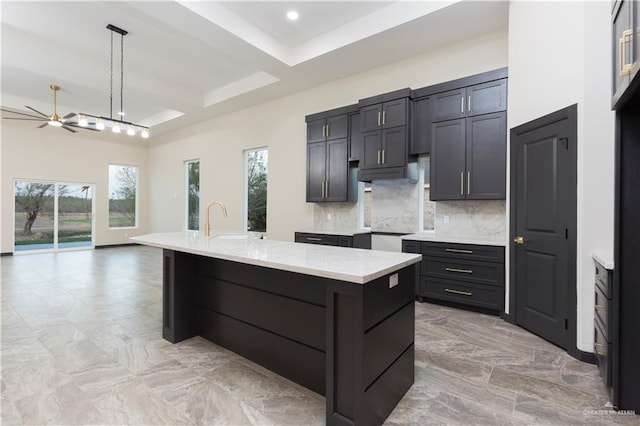 kitchen featuring light stone counters, hanging light fixtures, backsplash, and an island with sink