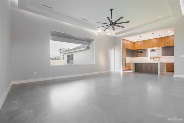 unfurnished living room featuring ceiling fan and a raised ceiling