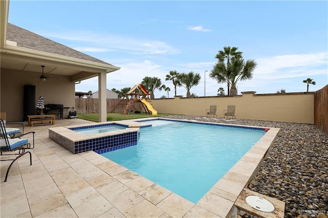 view of pool featuring a playground, ceiling fan, a patio area, and an in ground hot tub