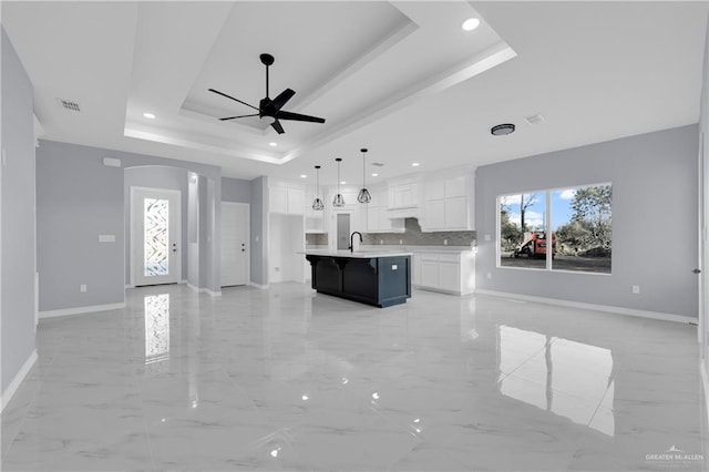 kitchen with white cabinetry, an island with sink, plenty of natural light, hanging light fixtures, and a raised ceiling