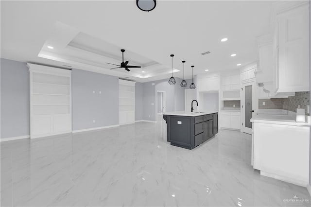 kitchen featuring white cabinetry, sink, decorative light fixtures, a raised ceiling, and an island with sink