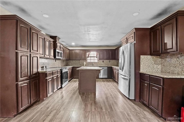 kitchen with dark brown cabinetry, stainless steel appliances, tasteful backsplash, a kitchen island, and light wood-type flooring