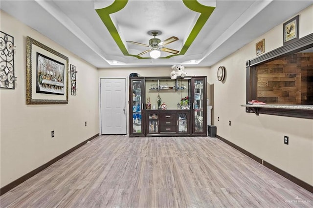 interior space with a raised ceiling, ceiling fan, and light hardwood / wood-style flooring