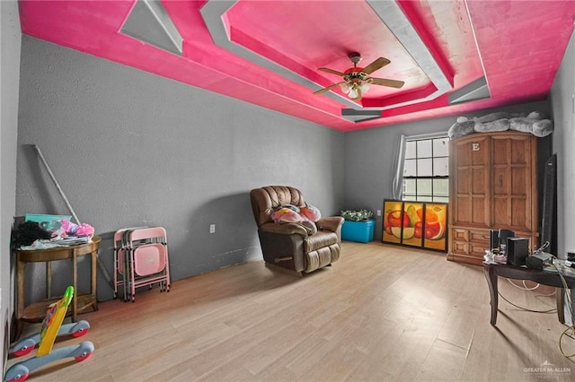 playroom with hardwood / wood-style floors, ceiling fan, and a raised ceiling