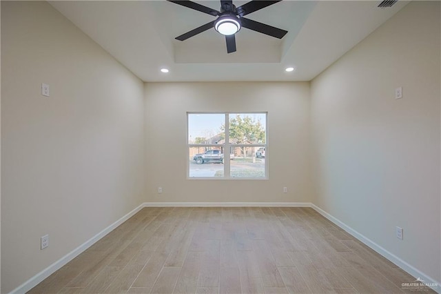 spare room with ceiling fan, a raised ceiling, and light wood-type flooring