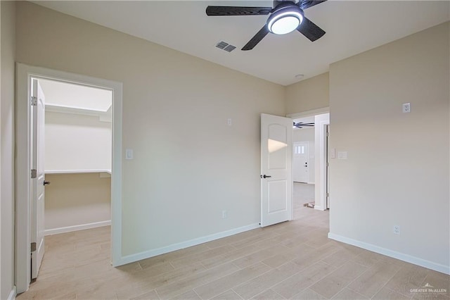 unfurnished bedroom with ceiling fan, a spacious closet, light wood-type flooring, and a closet