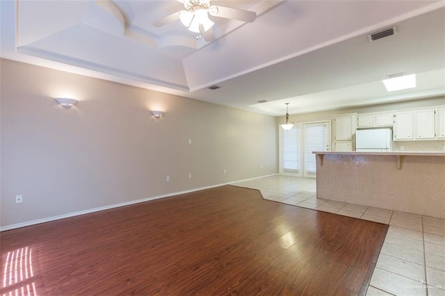 unfurnished living room with ceiling fan, light wood-type flooring, and a tray ceiling