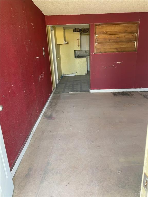 spare room featuring a textured ceiling, concrete flooring, and baseboards