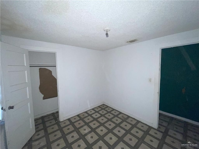 empty room featuring tile patterned floors, visible vents, baseboards, and a textured ceiling