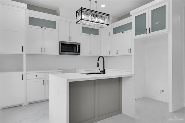 kitchen with pendant lighting, white cabinets, sink, and an island with sink