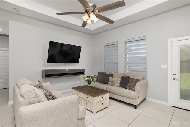 living area with light tile patterned floors, a ceiling fan, baseboards, a wealth of natural light, and a raised ceiling