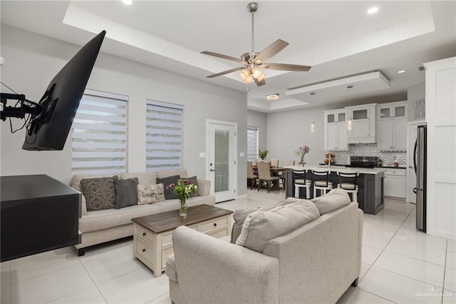 living area with light tile patterned floors, ceiling fan, a tray ceiling, and recessed lighting