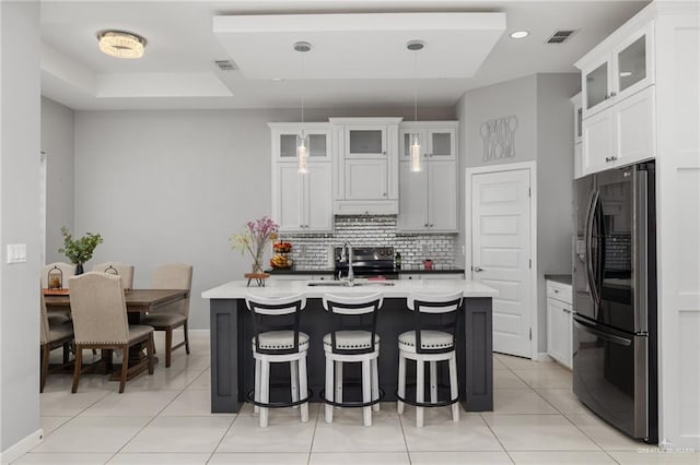 kitchen with tasteful backsplash, visible vents, a kitchen breakfast bar, freestanding refrigerator, and a sink